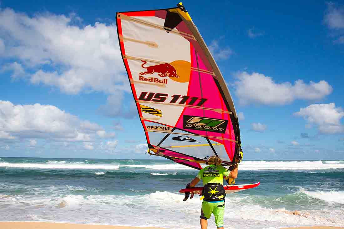 Robby Naish mit seiner Surf Ausrüstung am weg ins wasser